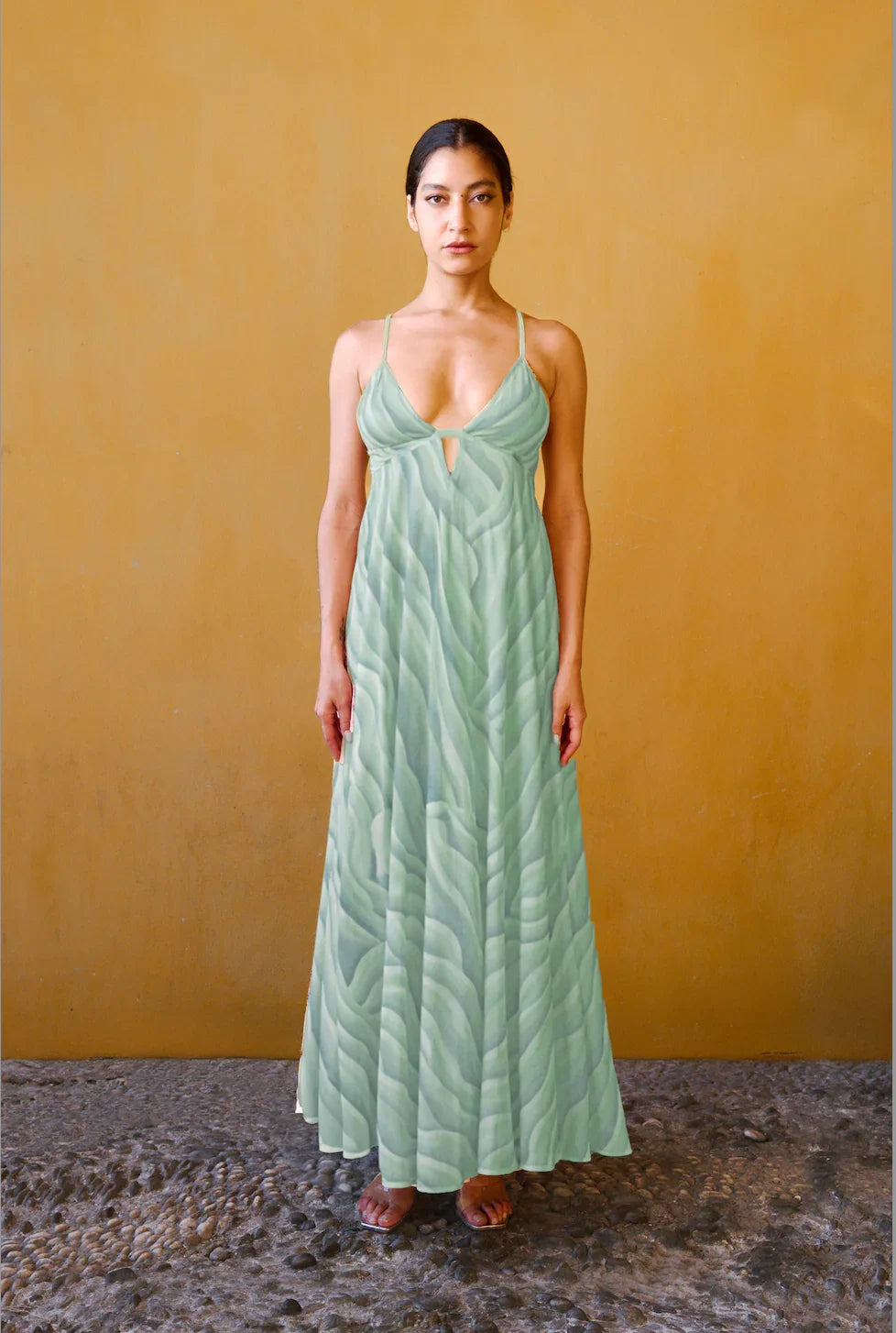 Woman in light green patterned maxi dress with thin straps, standing against mustard wall