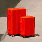 Ensemble de deux valises rigides GYL Intemporelle orange, tailles cabine et soute, posées sur sol béton. #couleur_orange foncé
