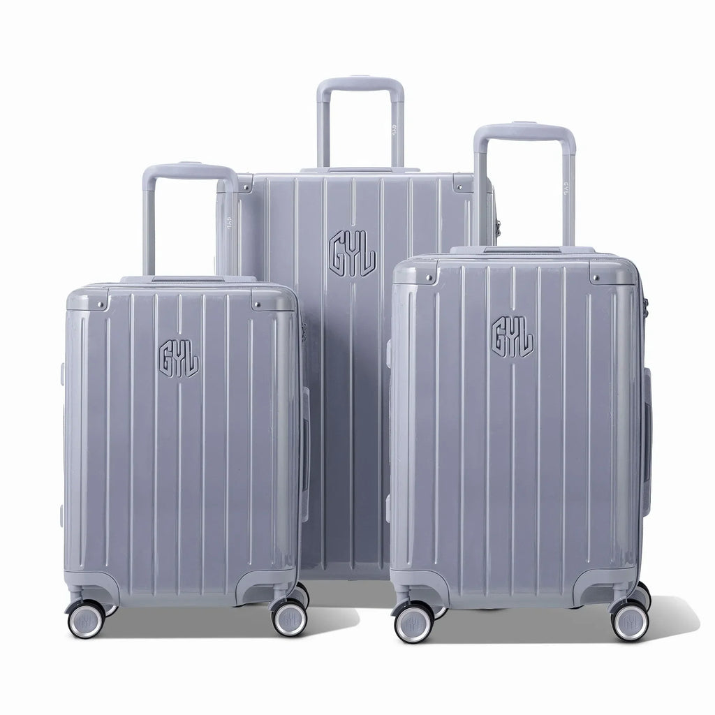 Trois valises rigides GYL Intemporelle argent, format cabine et soute, avec poignée trolley déployée.  #couleur_argent