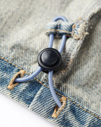 Gros plan sur un jean en denim bleu délavé avec cordon élastique réglable et bouton noir, matière 100 % coton, style décontracté et confortable pour femme.