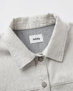 Col chemise en denim non teint couleur granit clair avec coutures apparentes et boutons métalliques, tissu 100% coton au toucher structuré et naturel.