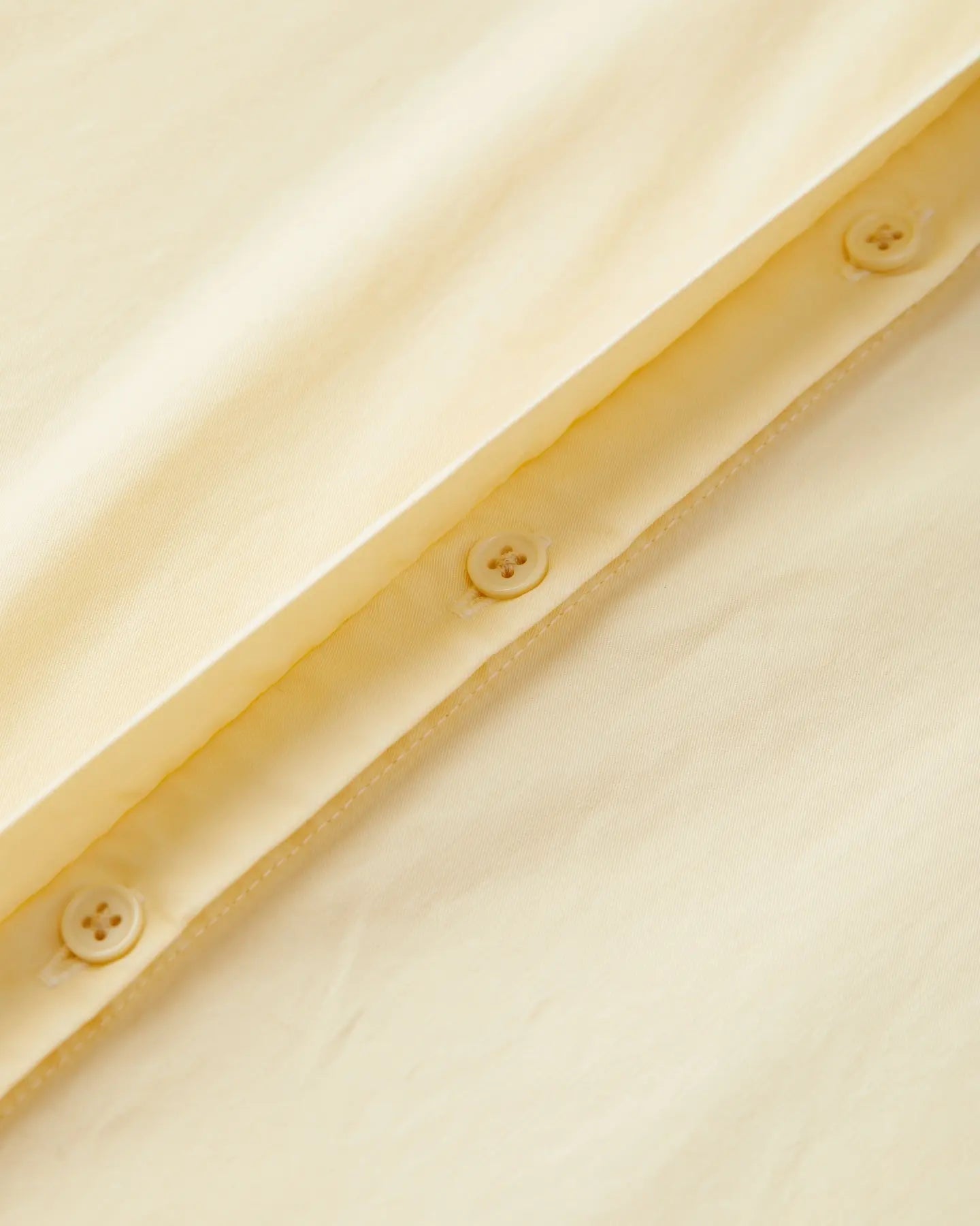 Détail en gros plan d'un tissu popeline vanille doux avec boutons, montrant la texture légère et la qualité du matériau idéal pour un pantalon d'été féminin.