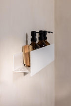 Duschablage SHEA mit Shampoo-Flaschen und einer Bürste auf einer weißen Wand, stilvolles und praktisches Badezimmerregal.