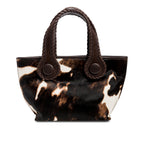 Dark brown and cream cow print pattern small tote bag with dark brown rope handles on a white background.