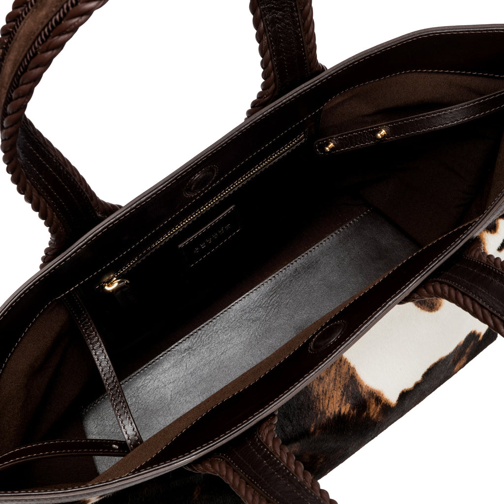 Close-up of a dark brown and cream cow print pattern bag with a dark brown interior. It has an inner pocket with zip. 