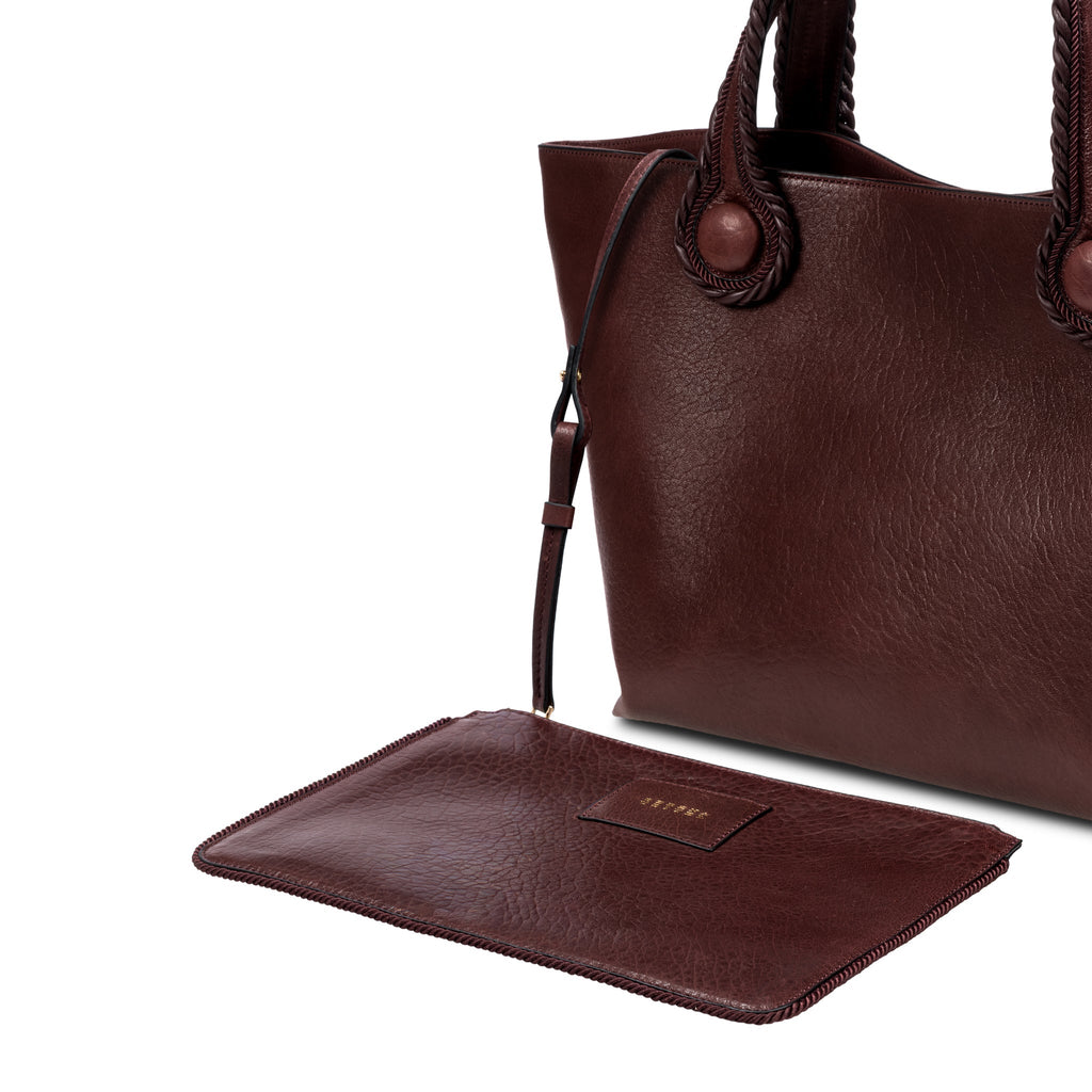 Burgundy leather in a shade of dark cherry tote bag with rope handles on a white background. It has a  removable inner bag in same color tone.