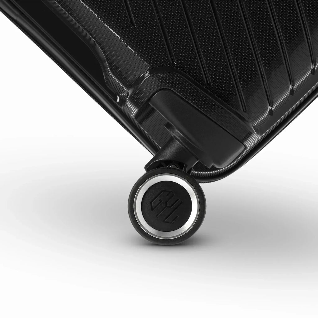 Détail de la roue avec logo GYL sur la valise Signature noire en polypropylène brillant. #couleur_noir