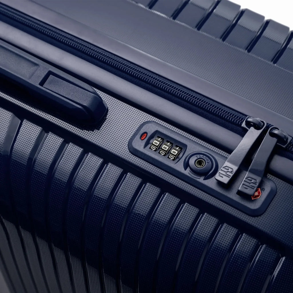 Détail de la serrure TSA intégrée et des curseurs sur la valise Signature marine. #couleur_marine
