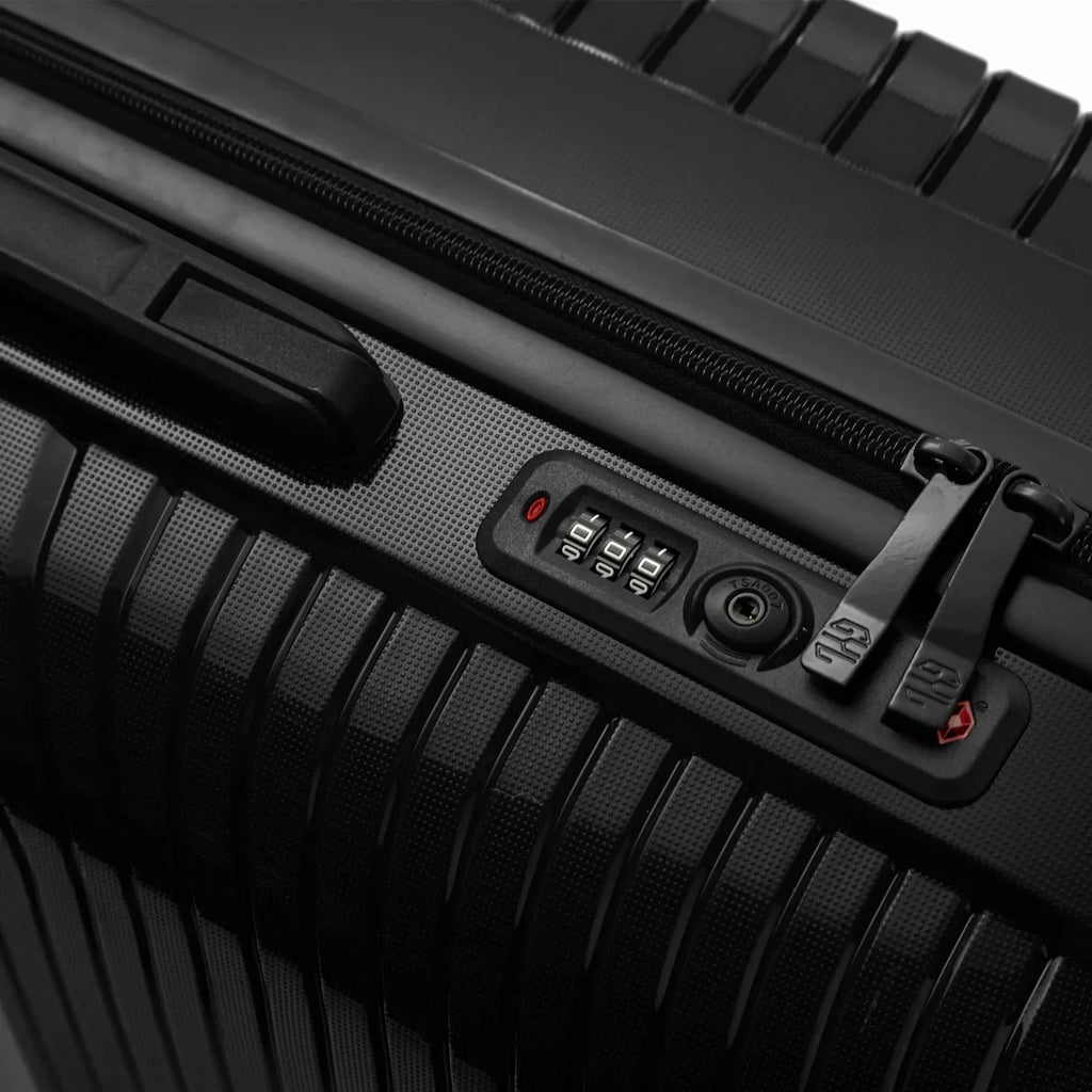 Détail de la serrure TSA intégrée et des curseurs sur la valise Signature noire. #couleur_noir