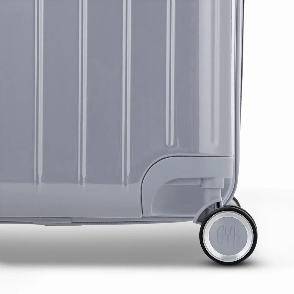 Détail de la roue et du logo GYL sur le bas de la valise trunk argent en polycarbonate brillant. #couleur_argent