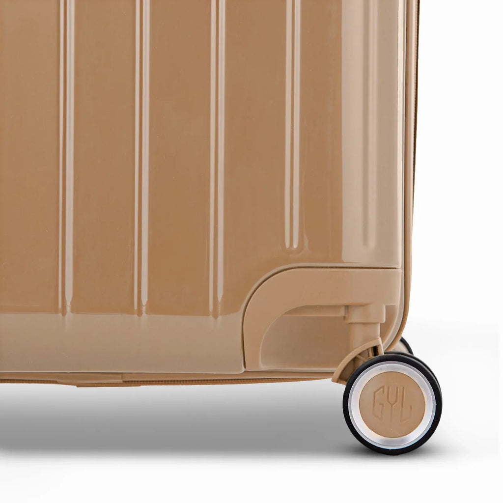 Détail de la roue et du logo GYL sur le bas de la valise trunk champagne en polycarbonate brillant. #couleur_champagne