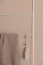 Handtuchleiter ESTINA mit einem beige Handtuch und einem natürlichen Reinigungsschwamm an einer weißen Wand.