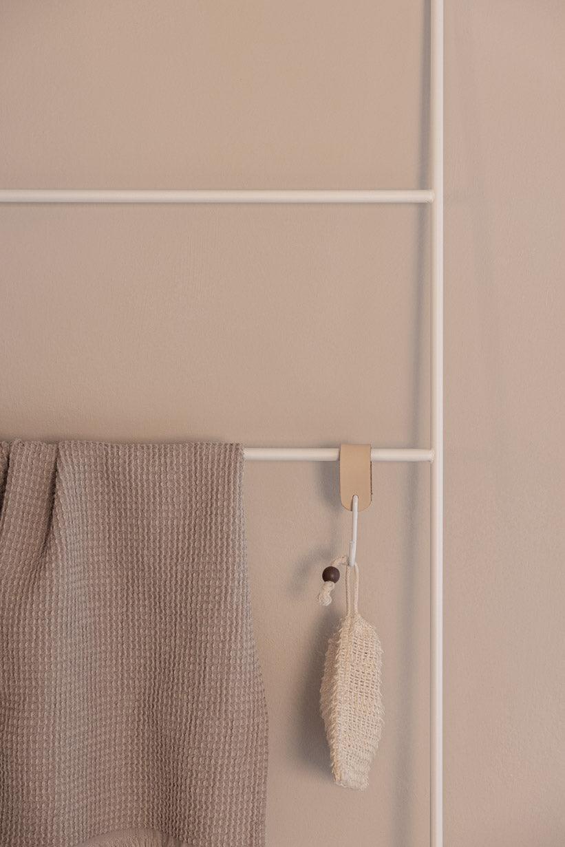 Handtuchleiter ESTINA mit einem beige Handtuch und einem natürlichen Reinigungsschwamm an einer weißen Wand.