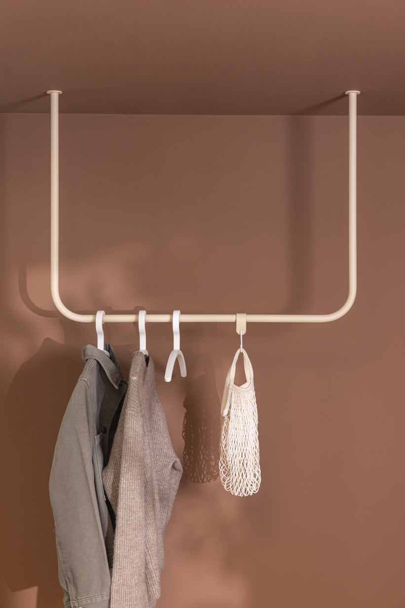Kleiderstange ENIO in abgerundeter Form mit Jacken und Accessoires an einer Wand montiert.