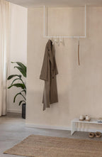 Moderne Kleiderstange RUBI mit minimalistischer Form, hält elegant einen Mantel in einem stilvollen Ankleidebereich.