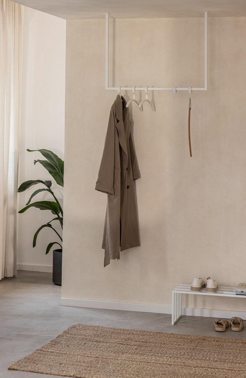 Moderne Kleiderstange RUBI mit minimalistischer Form, hält elegant einen Mantel in einem stilvollen Ankleidebereich.