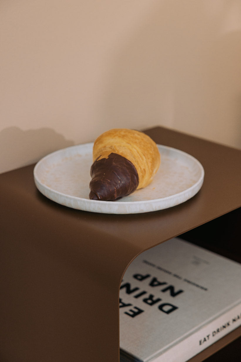 Stehender Nachttisch mit einer Servierplatte und einem Schokoladen-Croissant darauf.