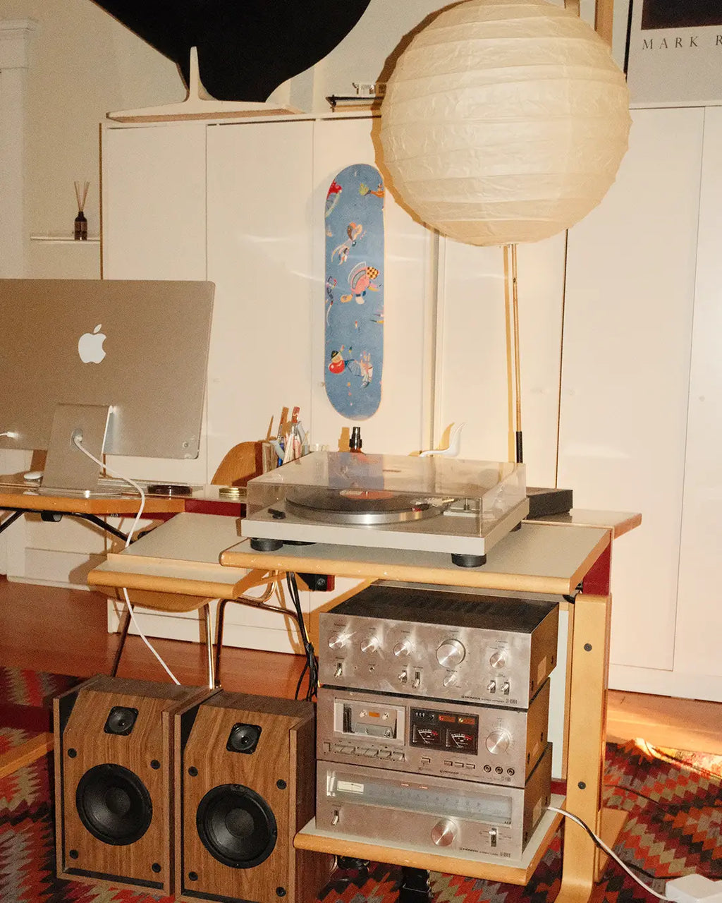 Interior home workspace featuring the ‘Blue Sky’ skateboard art edition by Wassily Kandinsky mounted on a white cabinet, styled alongside vintage Hi-Fi audio equipment, record player, wooden speakers, and a minimalist paper lantern.