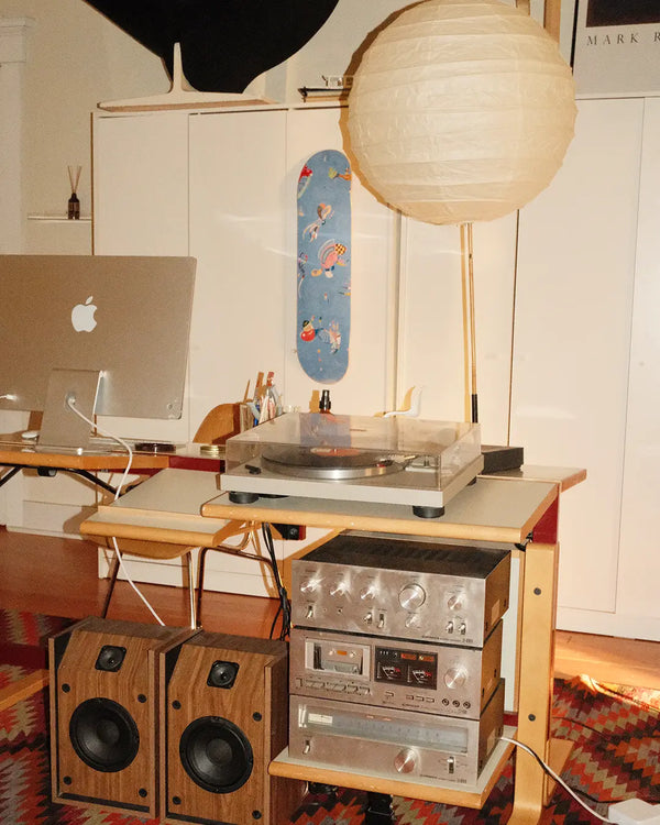 Interior home workspace featuring the ‘Blue Sky’ skateboard art edition by Wassily Kandinsky mounted on a white cabinet, styled alongside vintage Hi-Fi audio equipment, record player, wooden speakers, and a minimalist paper lantern.
