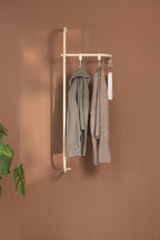 Garderobe TAMINA mit minimalistischer Metallstange und hängenden Kleidungsstücken an einer braunen Wand.