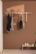 Garderobe TAMINA mit minimalistischer Metallstange und Kleidung an der Wand, stilvolles Design in warmen Farbtönen.