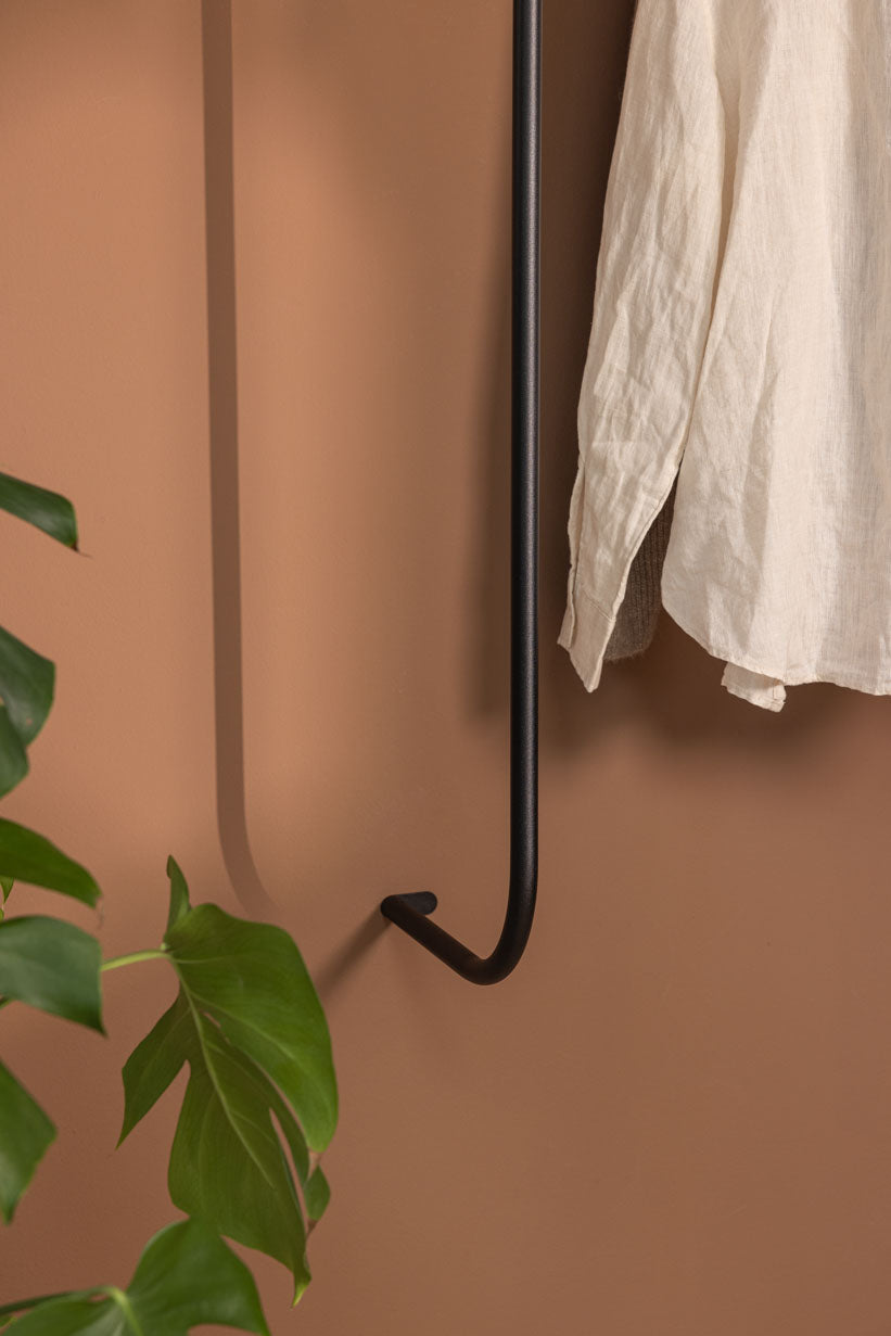 Garderobe TAMINA mit minimalistischen Metallstangen und aufgehängtem Kleidungsstück an einer wandfarbenen Wand.