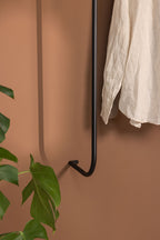 Garderobe TAMINA mit minimalistischen Metallstangen und aufgehängtem Kleidungsstück an einer wandfarbenen Wand.