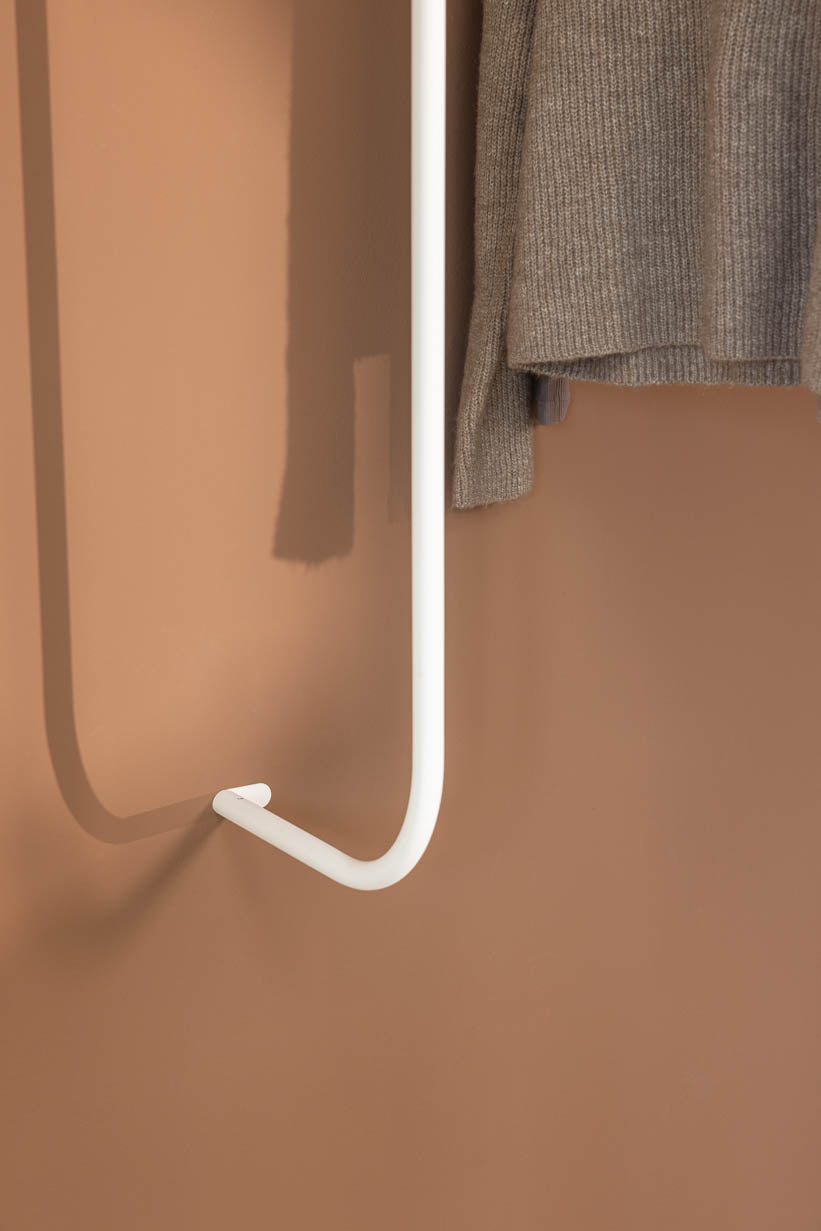 Detailansicht der Garderobe TAMINA mit grauem Pullover an einer weißen Metallstange.