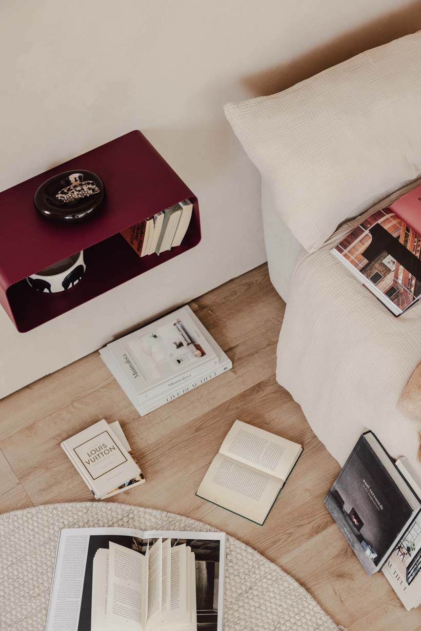 Hängender Nachttisch NELIO in modernem Design neben einem Sofa mit Bücherstapel auf dem Boden.