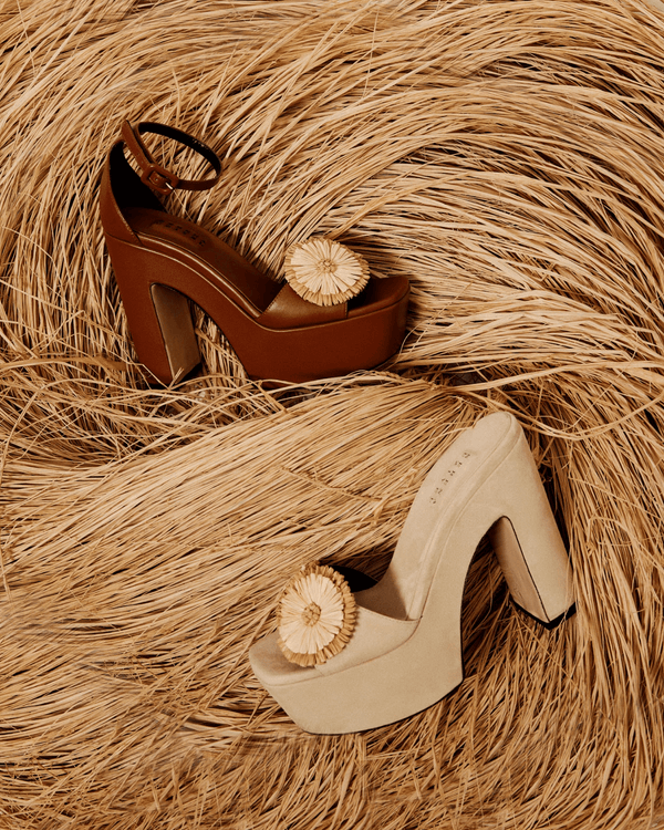 Narcissa Sand Platform Sandals in tan and beige suede with floral accents, set against a textured hay background.