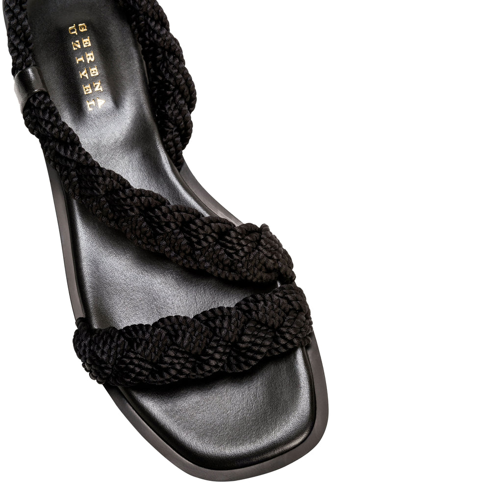 Ronda Black Flat Asymmetric Sandal featuring braided black straps and a sleek leather sole, perfect for summer wear.