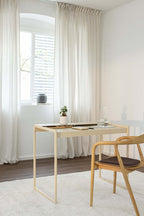 Schreibtisch DONNA in einem modernen Raum mit Stuhl und Pflanzen auf dem Tisch, Fenster mit Vorhängen im Hintergrund.
